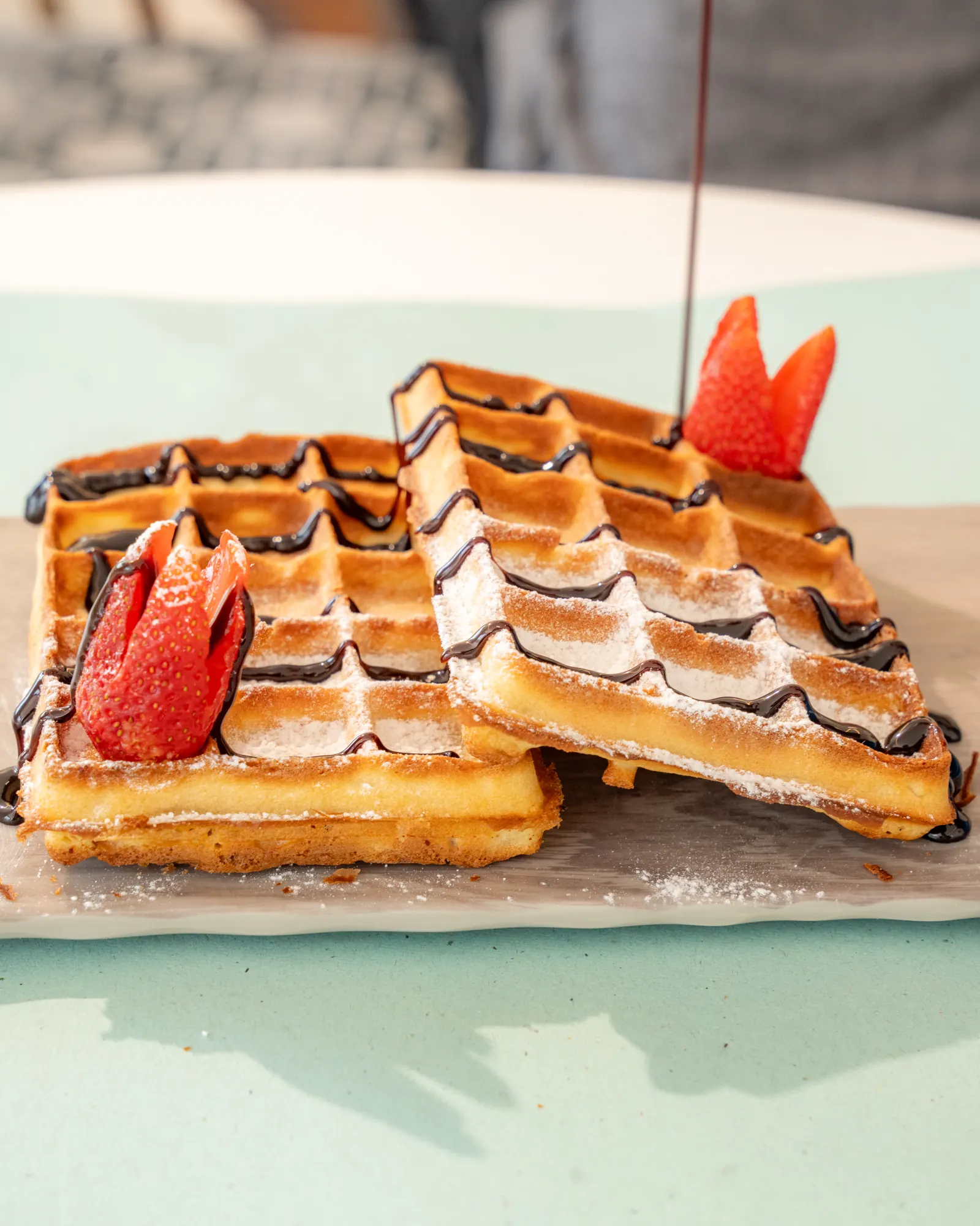 Waffles dusted with sugar, topped with strawberries and a chocolate drizzle