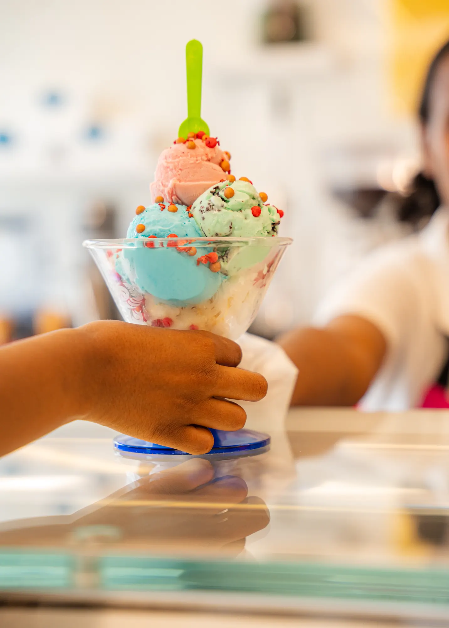 A three-scoop sundae with sprinkles, handed over the counter