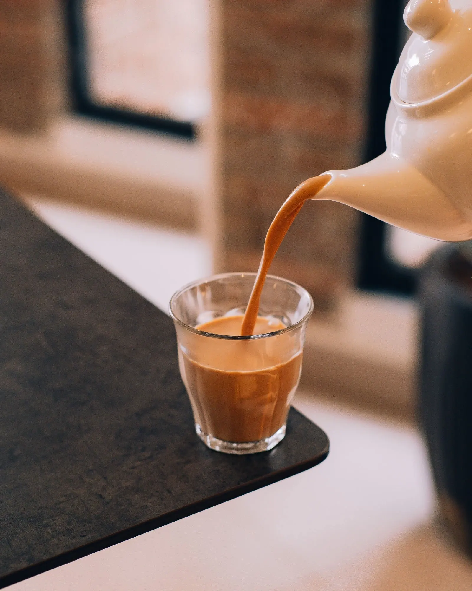 Milk tea poured from a white teapot into a glass