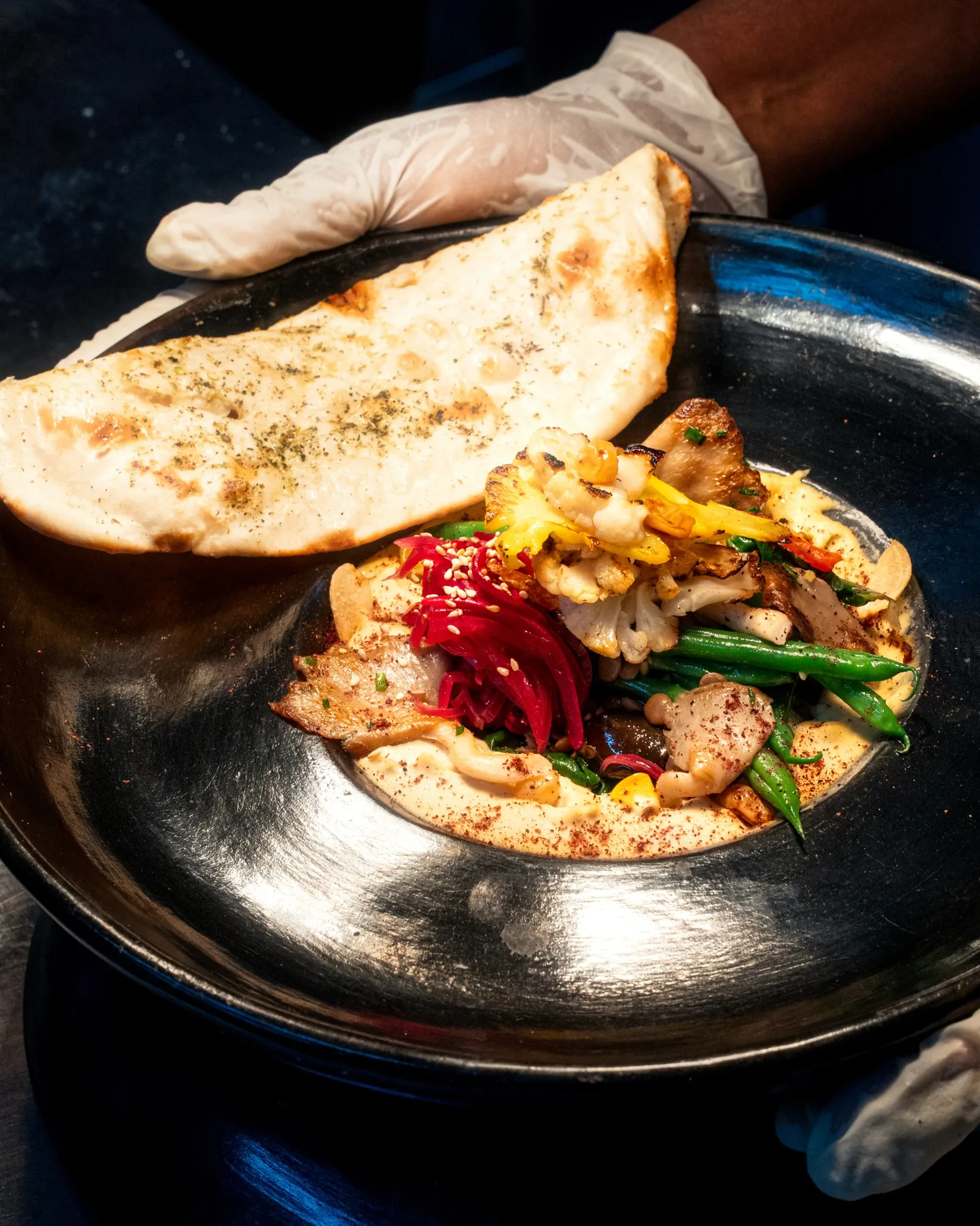 A gloved server presenting the mezze plate with flatbread