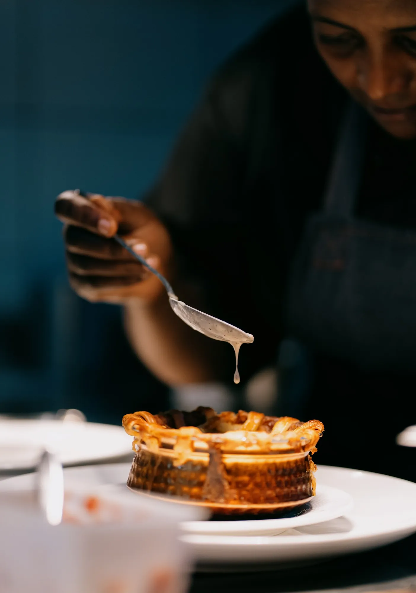A chef spooning sauce over a baked pie at the pass