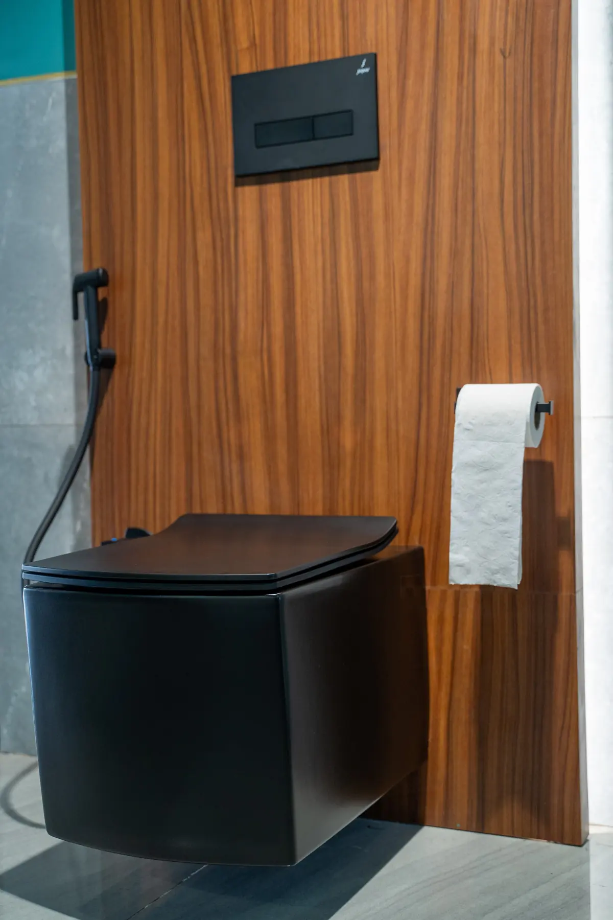 A matte black toilet against a walnut wall